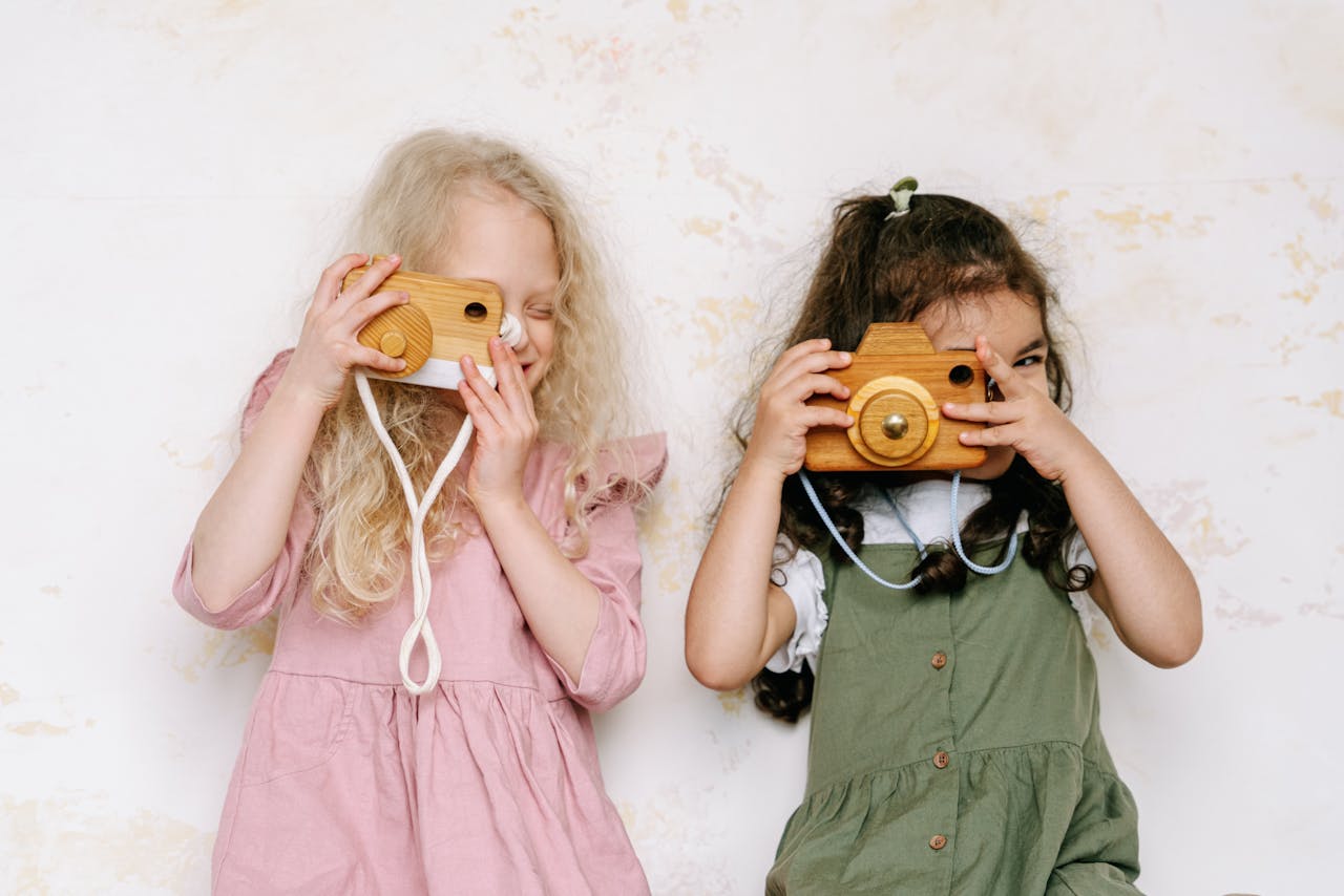 Two young girls playing with wooden cameras, showcasing imagination and creativity indoors.